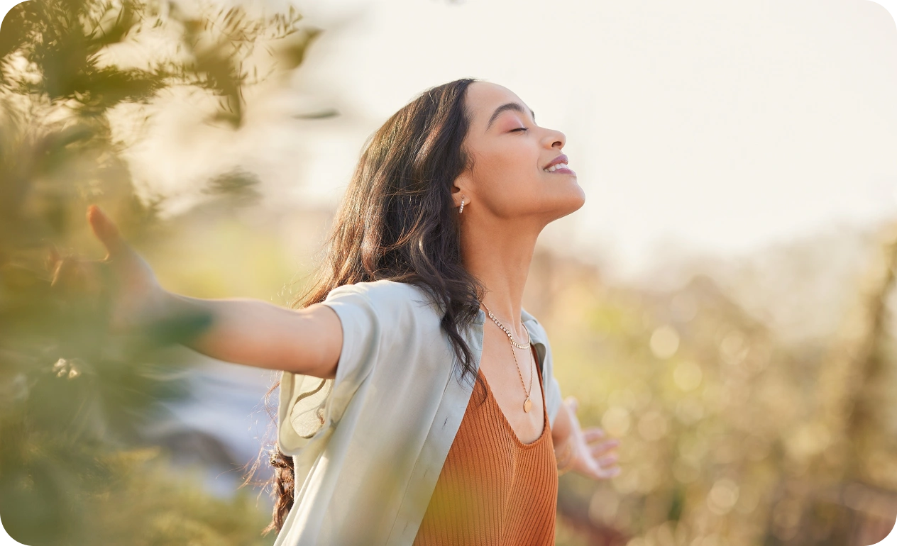 Mujer con los brazos abiertos disfrutando al aire libre bajo la luz del sol